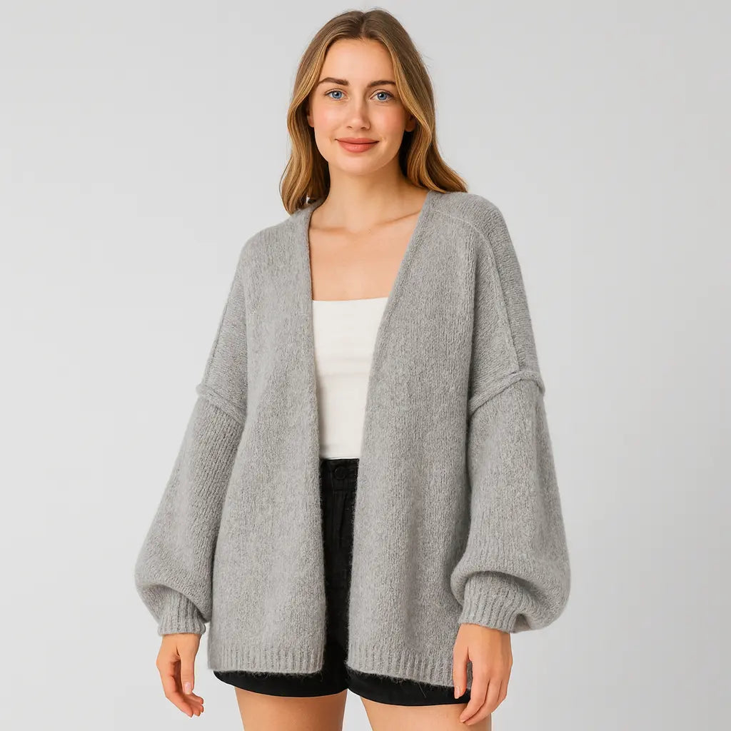 Woman wearing a gray cardigan over a white top and black shorts on a light gray background
