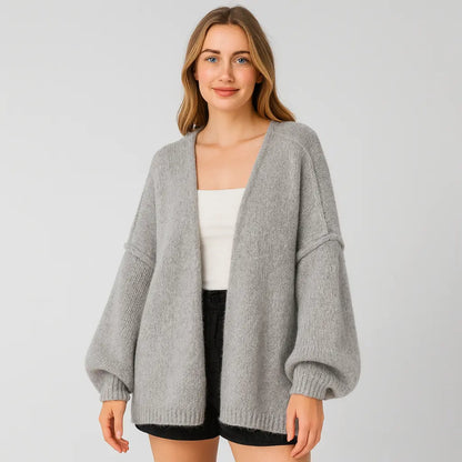 Woman wearing a gray cardigan over a white top and black shorts on a light gray background